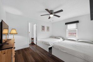 Et soveværelse med to senge, en ventilator, et vindue med udsigt og et skrivebord med lampe.