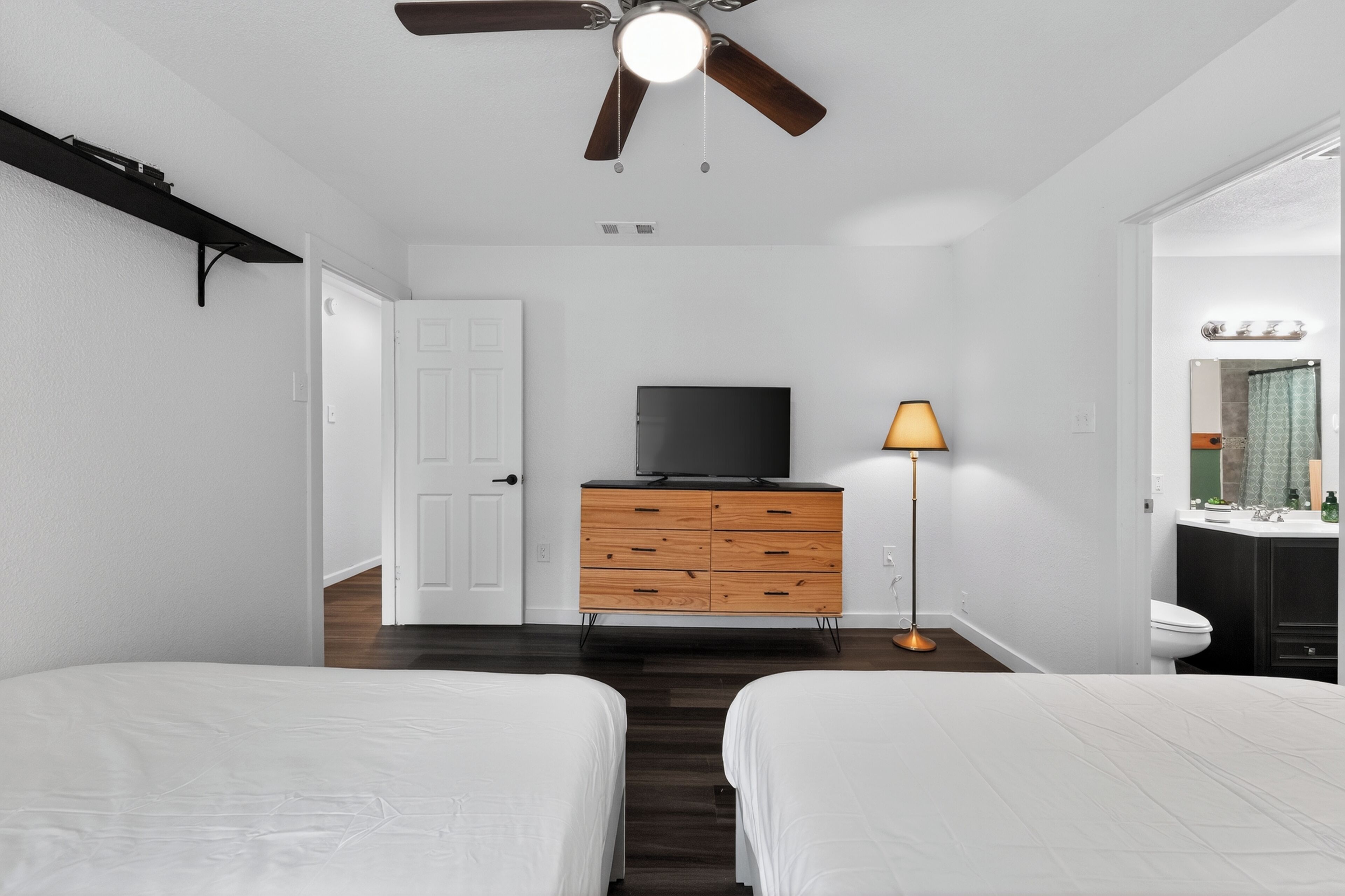 Ein Schlafzimmer mit zwei Betten, einem Fernseher, einem Schminktisch, einer Lampe und einem Deckenventilator.