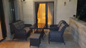 A patio area with wicker furniture, a glass door leading to a room, and a small plant on the right.