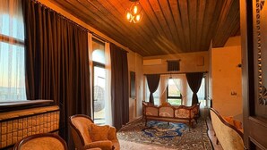 Una stanza con travi a vista in legno, un letto grande con copripiumino decorato, due poltrone e un tappeto ornamentale.