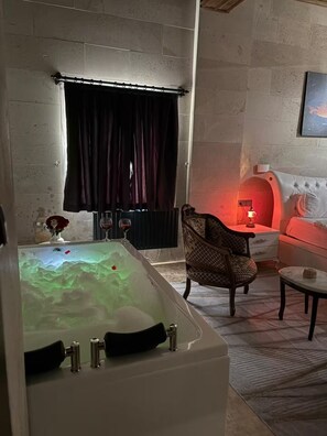 Una habitación con una bañera grande, un sillón estampado, una mesita pequeña y un sofá.