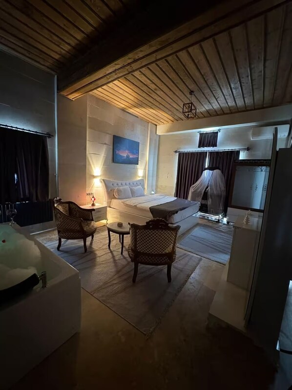 Una habitación con cama, dos sillas, una mesita, bañera y un cuadro en la pared.