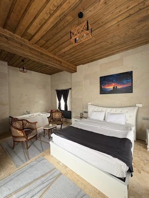 Un dormitorio con techo de madera, una cama, un cuadro, una bañera y dos sillas.
