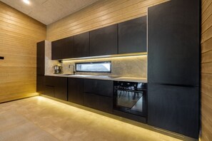A modern kitchen with dark cabinetry, a built-in oven, and a stainless steel countertop. - Villa Noel A | Premium 4BR Villa | Near Ski Lifts (Kittilä)