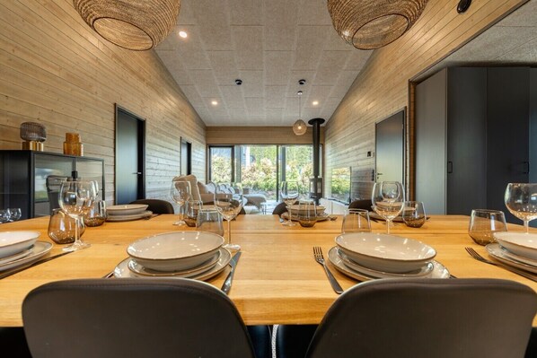 A modern dining room with a long table set for a meal, wooden walls, and large windows.