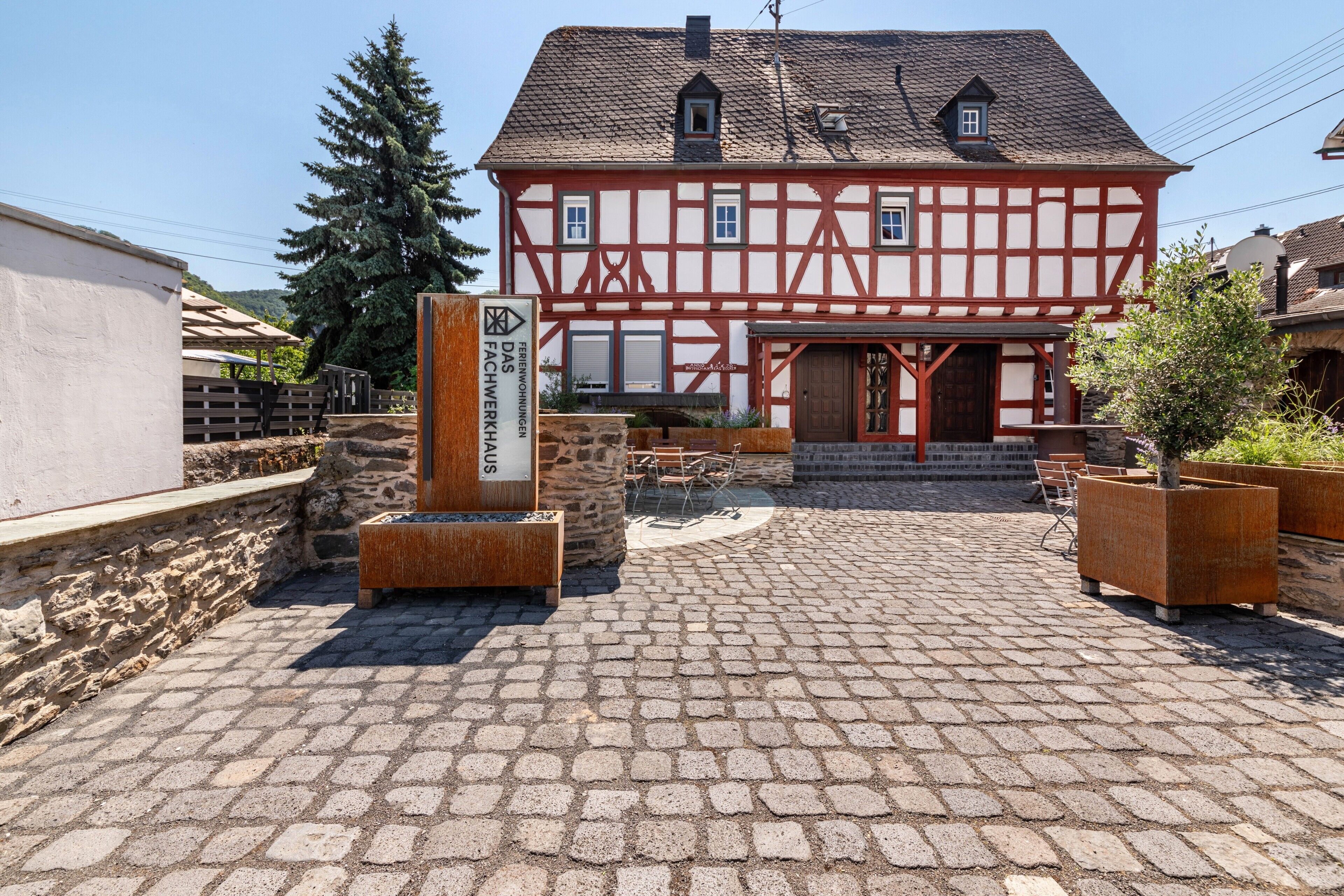 A traditional half-timbered building with a cobblestone courtyard, stone benches, and a sign indicating a restaurant.