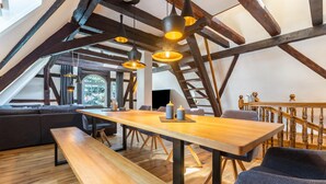 Ein Loft-Zimmer mit freiliegenden Holzbalken, einem Holztisch, Bänken und einer Couch.