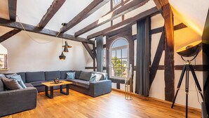 Ein Loft-Zimmer mit freiliegenden Holzbalken, einem dunkelgrauen Sofa, einem Holztisch und einer Dreibeinlampe.
