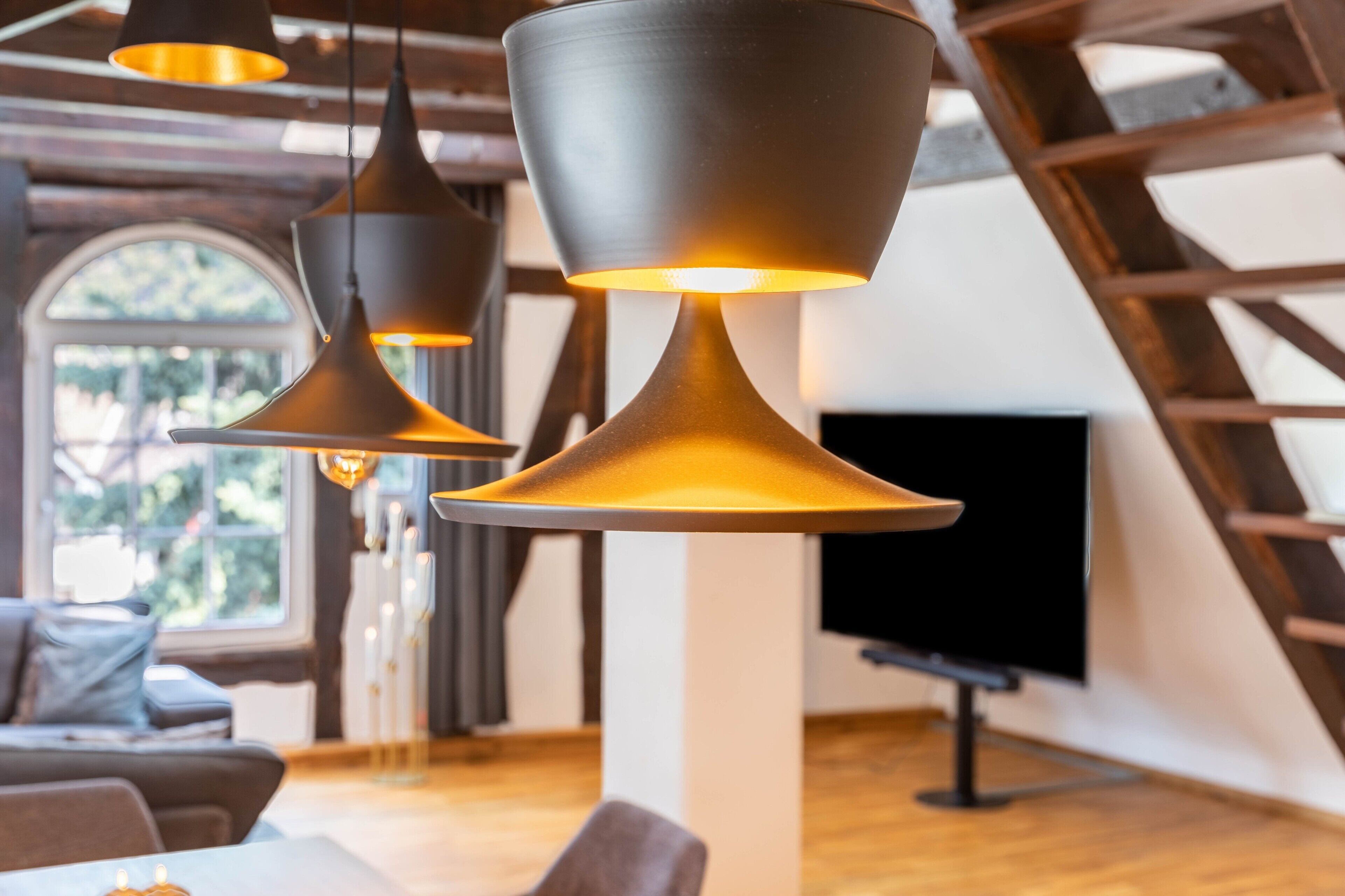A modern interior with hanging pendant lights, a flat-screen TV, and a wooden ceiling structure.