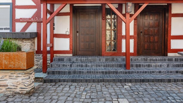 Ein Gebäude mit einer traditionellen Fachwerkfassade, zwei Holztüren und Steinstufen, die zum Eingang führen.