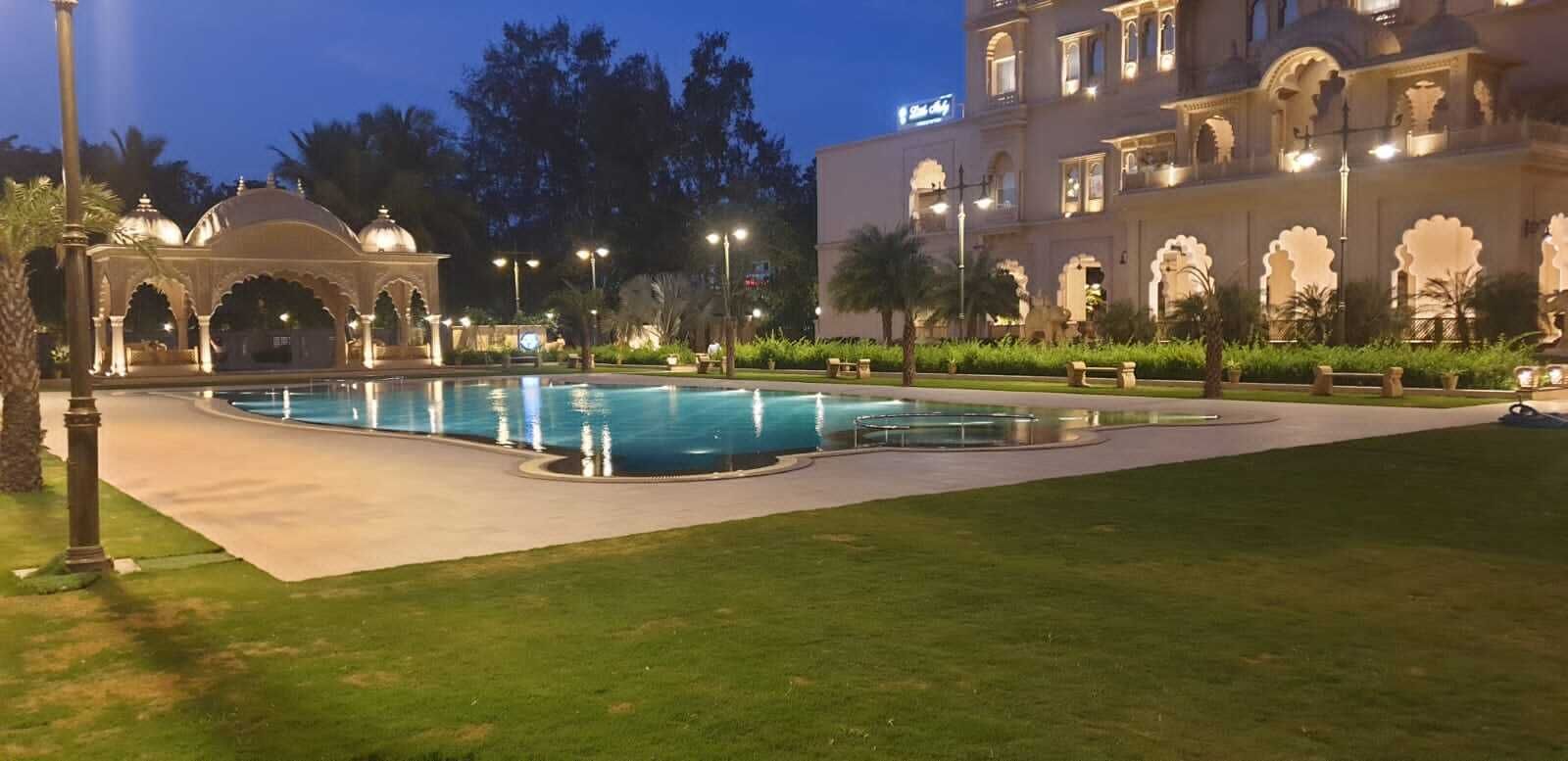 A swimming pool with a surrounding garden, a large building with arches, and a sign indicating a hotel.