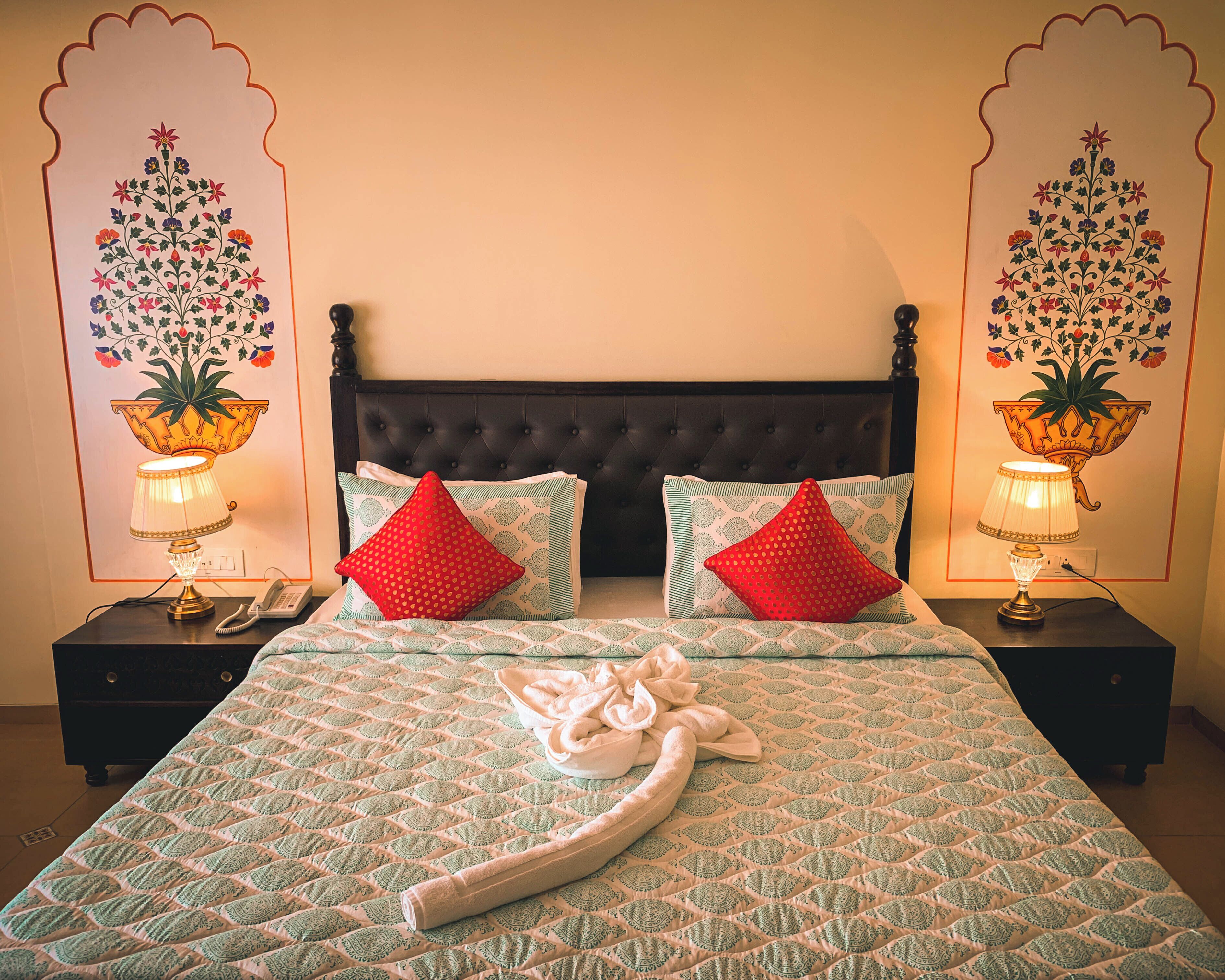 Un lit avec une couvre-lit à motifs, deux oreillers rouges, une serviette et deux lampes de chevet ornées de vases décoratifs.