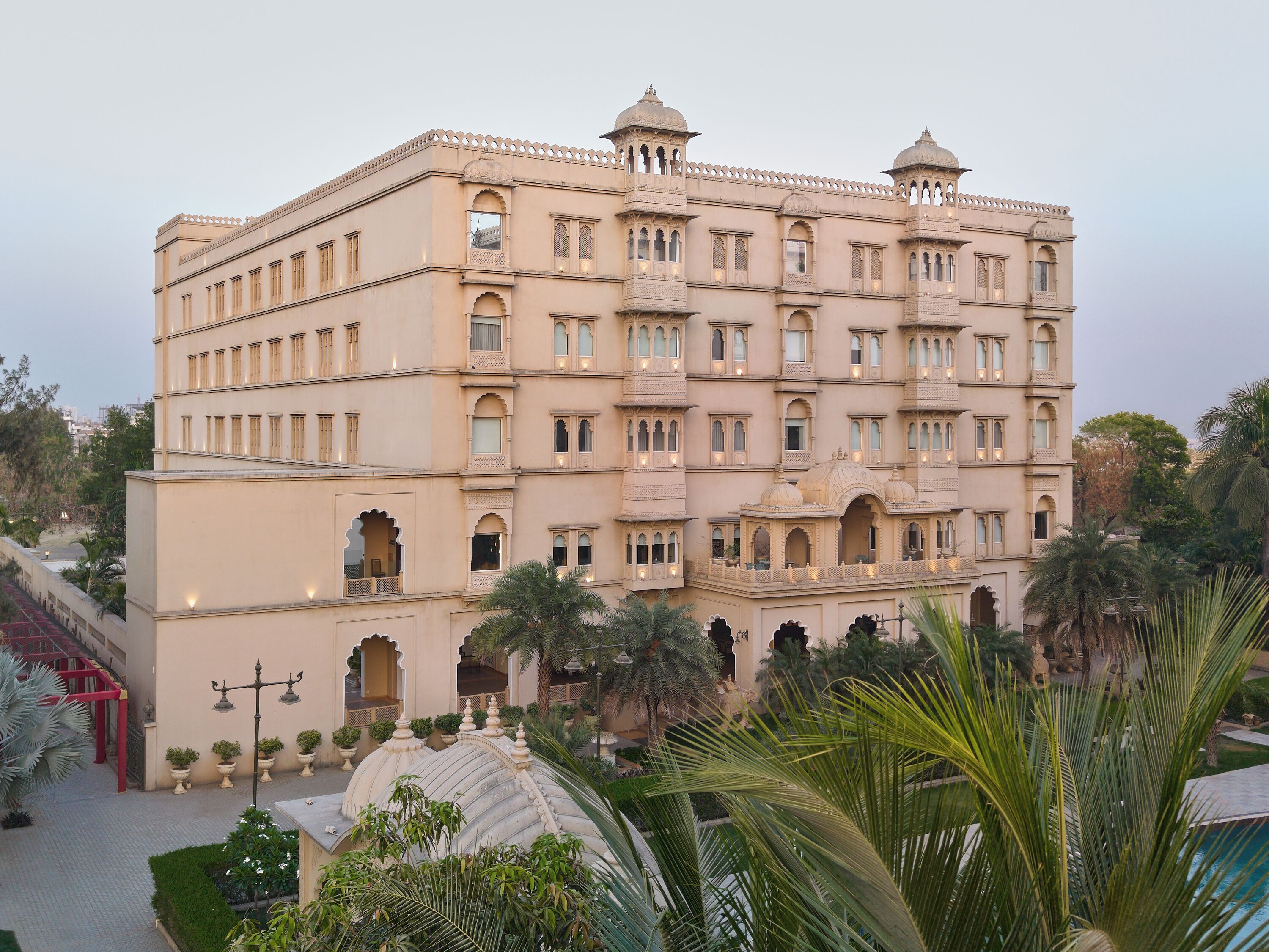 A multi-story building with arched windows and balconies, surrounded by palm trees and a well-maintained garden.