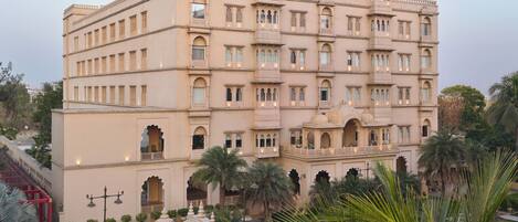 A multi-story building with arched windows and balconies, surrounded by palm trees and a well-maintained garden.