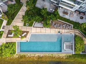 Eine Vogelperspektive eines modernen Hotels mit großem Schwimmbad, Sitzgelegenheiten im Freien und üppiger Bepflanzung.