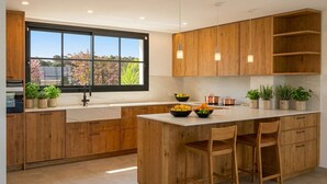 A modern kitchen with wooden cabinets, a large window, and a central island with chairs. - Villa Las Golondrinas New 100% July 2026  20 minutes walk from Sitges Beaches (Sitges)