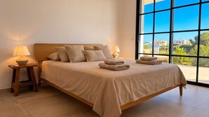 Ein Bett mit Holz-Kopfstück, zwei Nachttischlampen und Blick durch große Fenster.