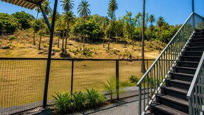 A view from a covered area with a staircase leading to a higher level, overlooking a natural landscape with palm trees and a body of water. - Bungalow Seven (Mount Abu)