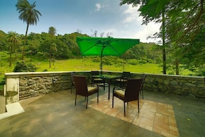 Une terrasse extérieure avec des murs en pierre, une table avec des chaises et un parasol vert.