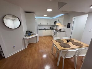 A compact kitchen with white cabinets, a central island, and a dining area with a wooden table and chairs. - Amazing 2BR Basement Suite (Langley Township)