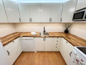 A compact kitchen with white cabinets, a wooden countertop, a dishwasher, and a microwave. - Amazing 2BR Basement Suite (Langley Township)