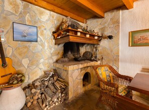 A rustic stone fireplace with a wooden mantel, a guitar, a wicker chair, and a pile of firewood. - Villa Danci (Mali Losinj)