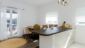 Una cucina moderna con isola centrale, zona pranzo con sedie e vista attraverso una porta in vetro.