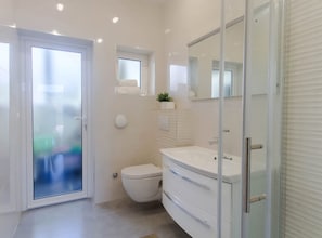 A modern bathroom with a toilet, a vanity with drawers, a glass shower enclosure, and a frosted glass door.