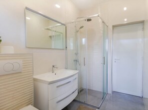 A modern bathroom with a glass-enclosed shower, a white vanity, and a large mirror.