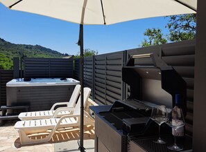 Un patio exterior con jacuzzi, parrilla, sillas de lounge y una botella de vino.