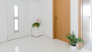 Una stanza con una porta bianca, una porta in legno, una cassettiera bianca con una pianta e un vaso di fiori.