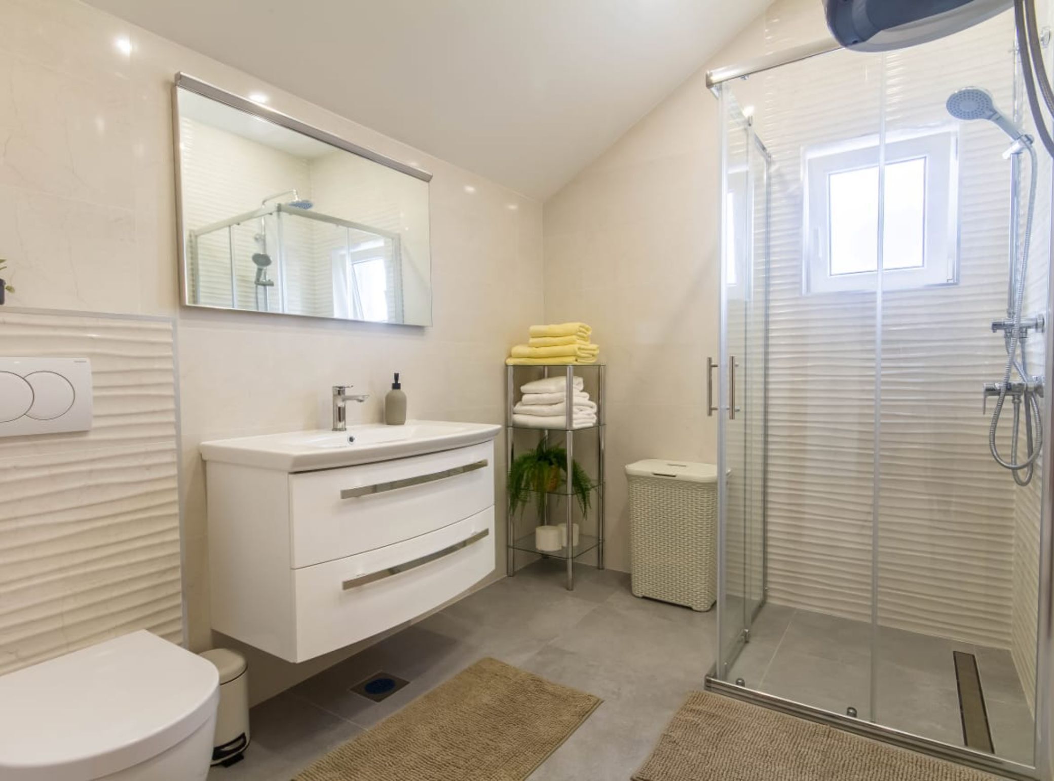 Un baño moderno con cabina de ducha de vidrio, tocador blanco, espejo y perchero.