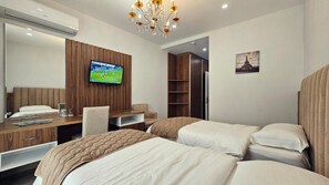 A hotel room with two beds, a desk with a TV, a wardrobe, and a chandelier.