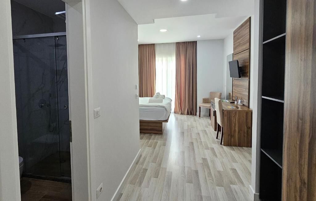 A modern hotel room with a bed, a desk, a TV, and a shower area.