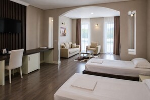 A hotel room with a desk, two beds, a sofa, and a TV.