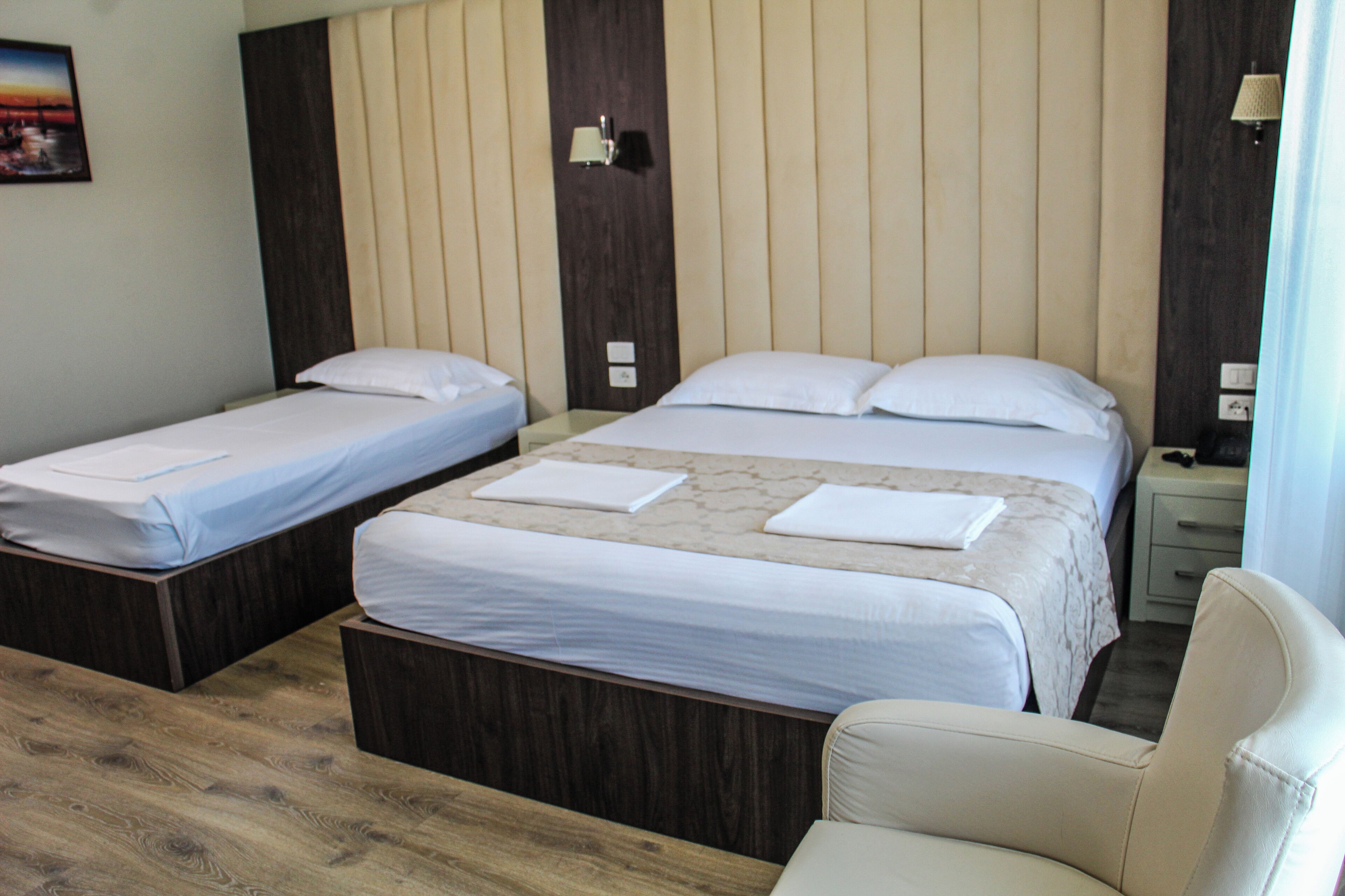 A hotel room with two single beds, a double bed, a wooden floor, a nightstand, and a chair.