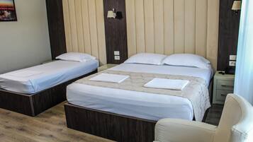 A hotel room with two single beds, a double bed, a wooden floor, a nightstand, and a chair.