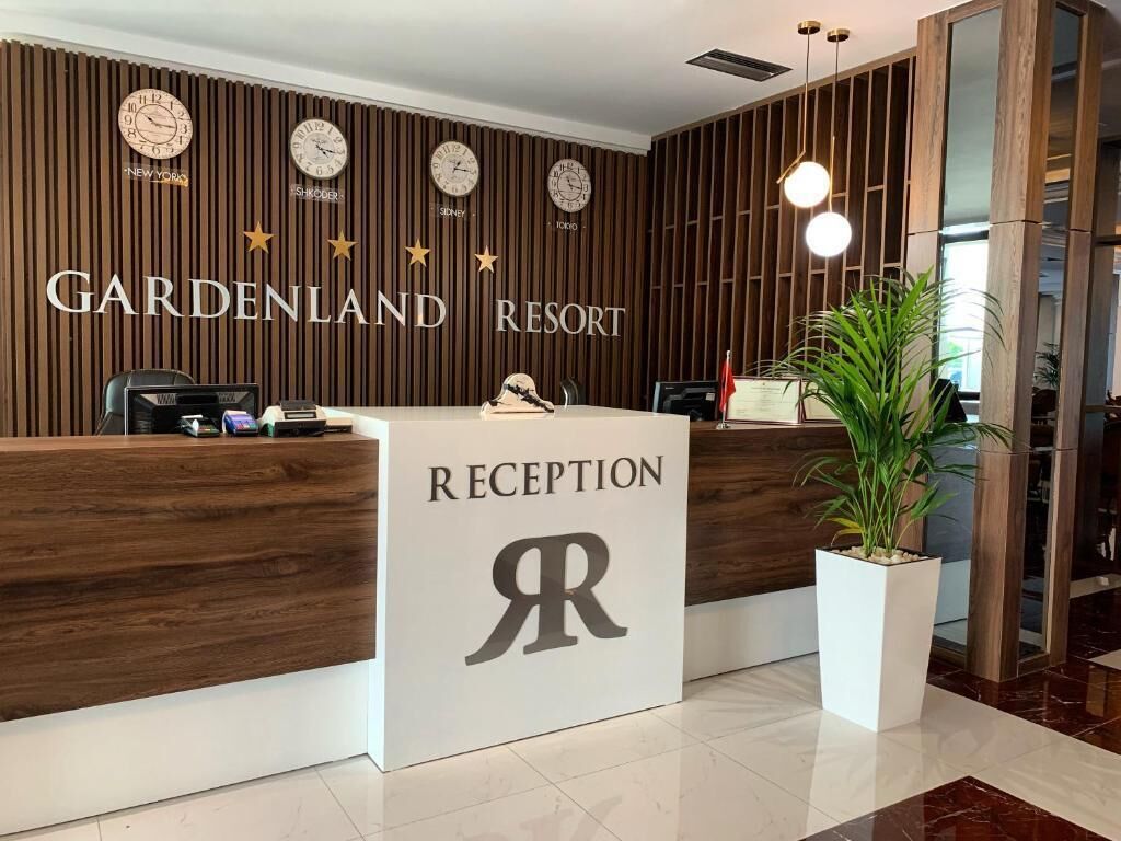 A reception desk at Gardenland Resort with clocks, a logo, and a potted plant.