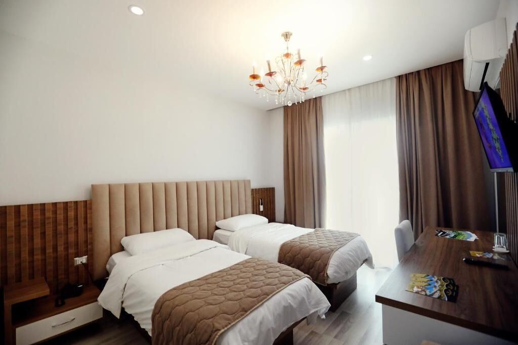 A hotel room with two beds, a wooden headboard, a desk with a chair, a television, and a chandelier.