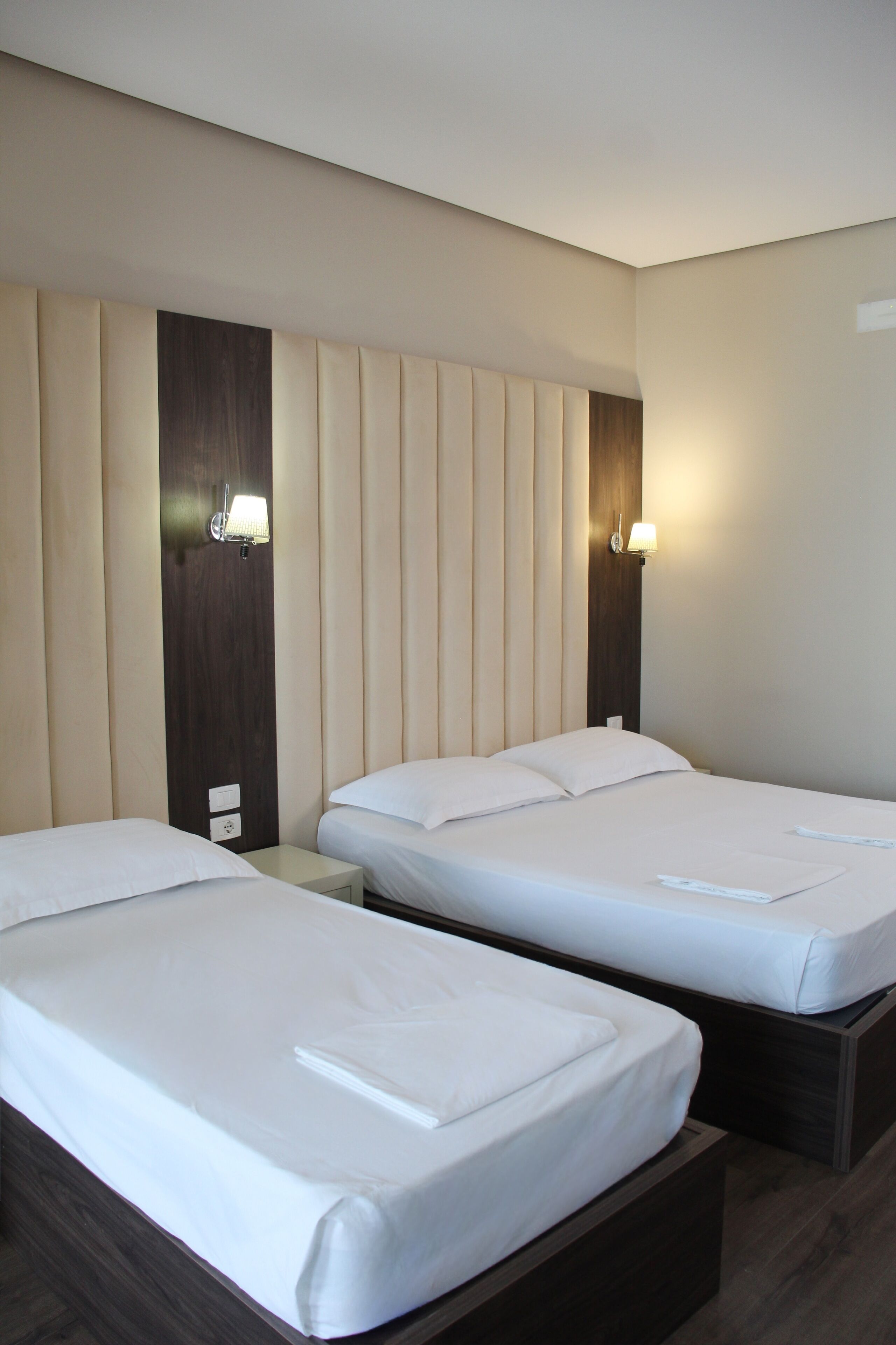 A hotel room with two beds, a wooden headboard, bedside lamps, and a nightstand.