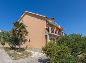 A two-story building with a balcony, a stone foundation, and a clear blue sky. - Andrija Sea View Apartments (Rab)