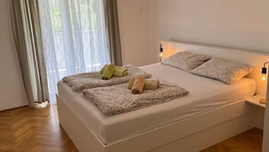 A neatly made bed with floral bedding, a bedside lamp, and a window with sheer curtains.