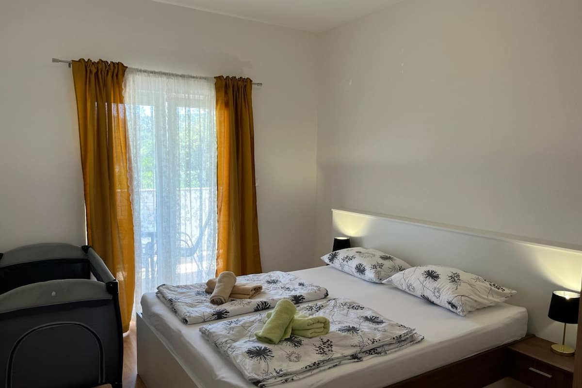 A hotel room with a bed, a chair, a lamp, and a window with curtains.