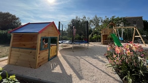 A wooden playhouse, a trampoline, and a wooden swing set in a garden.
