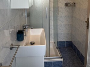 A bathroom with a glass-enclosed shower, a white sink with a faucet, and a blue container on the counter. - Apartments Poldan Rab (Lopar)