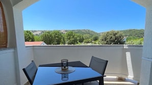 A balcony with a table and chairs, a glass on the table, and a view of a green landscape.