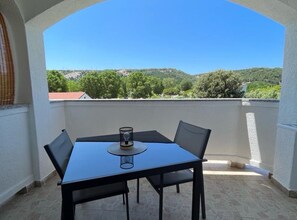 Ein Balkon mit Tisch und Stühlen, ein Glas auf dem Tisch und Blick auf eine grüne Landschaft.