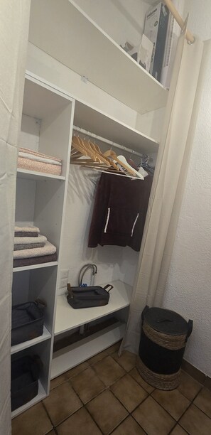A walk-in closet with shelves, a hanging rack, and a small shelf with a bag and a bottle. - Studio on hiking trails and paths.  Ideal for a couple. (Les Gets)