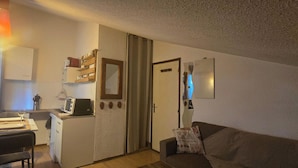 A compact living space with a kitchenette, a dining area, a sofa, and a door leading to another room. - Studio on hiking trails and paths.  Ideal for a couple. (Les Gets)