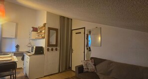 A compact living space with a kitchenette, a dining area, a sofa, and a door leading to another room. - Studio on hiking trails and paths.  Ideal for a couple. (Les Gets)